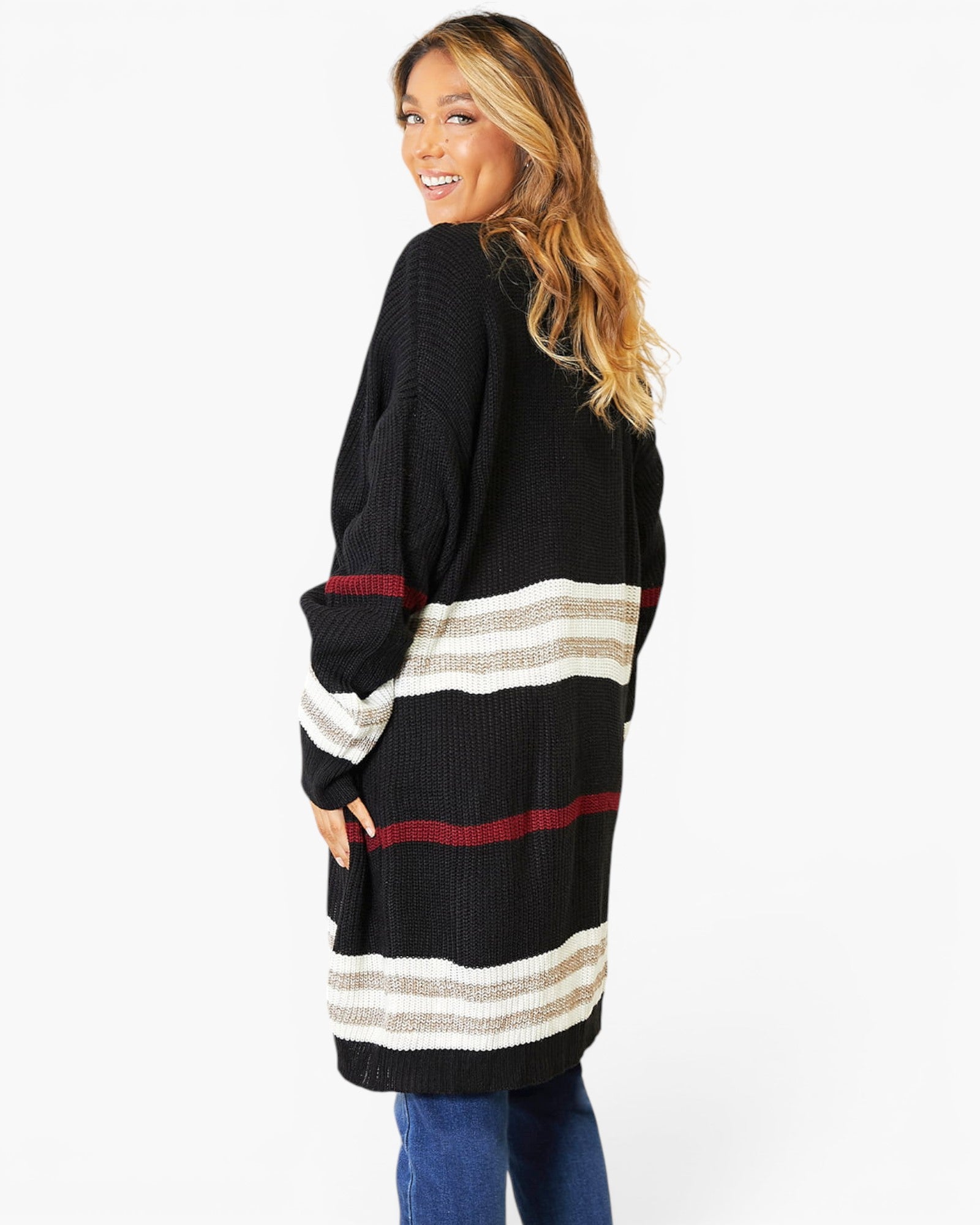 A woman modeling a black knit cardigan with horizontal stripes in cream, gray, and burgundy, paired with blue jeans against a plain white studio background.