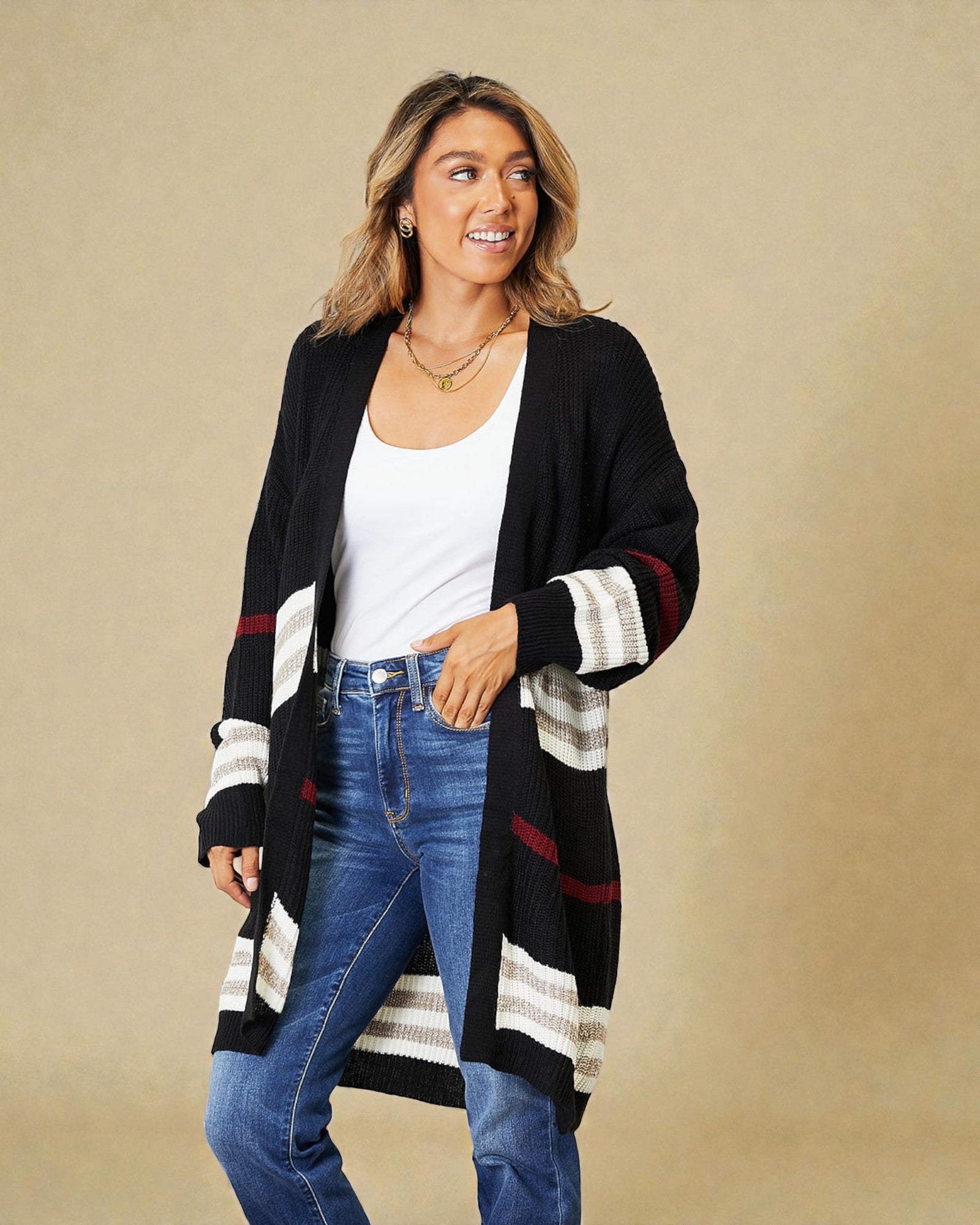 Woman wearing a black cardigan with white and red stripes, white shirt, and blue jeans on a beige background