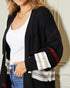 Woman wearing a black cardigan with colorful sleeves, white top, and blue jeans indoors.