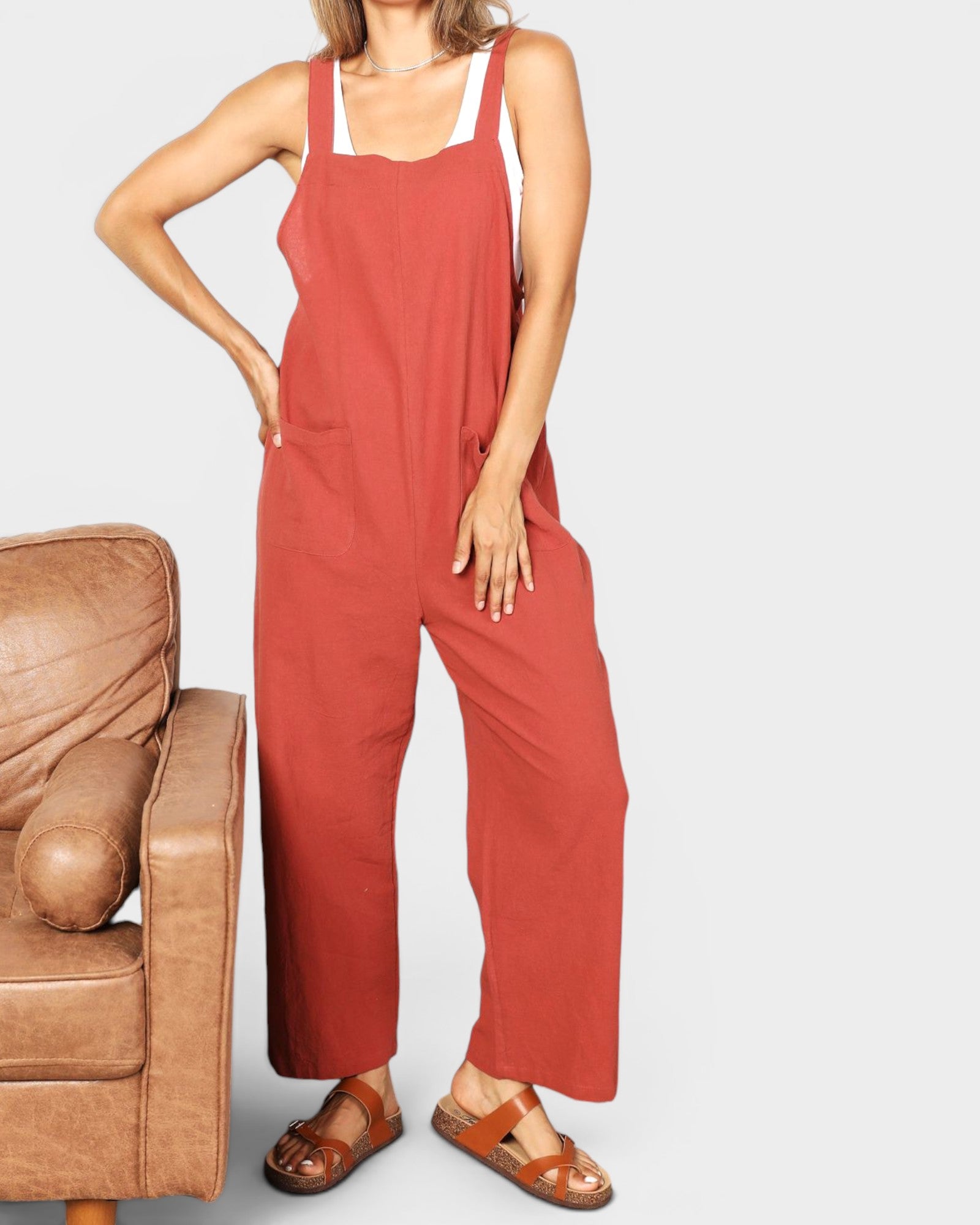 Person wearing red overalls standing next to a brown leather chair on a white background