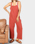 Person wearing red overalls standing next to a brown leather chair on a white background