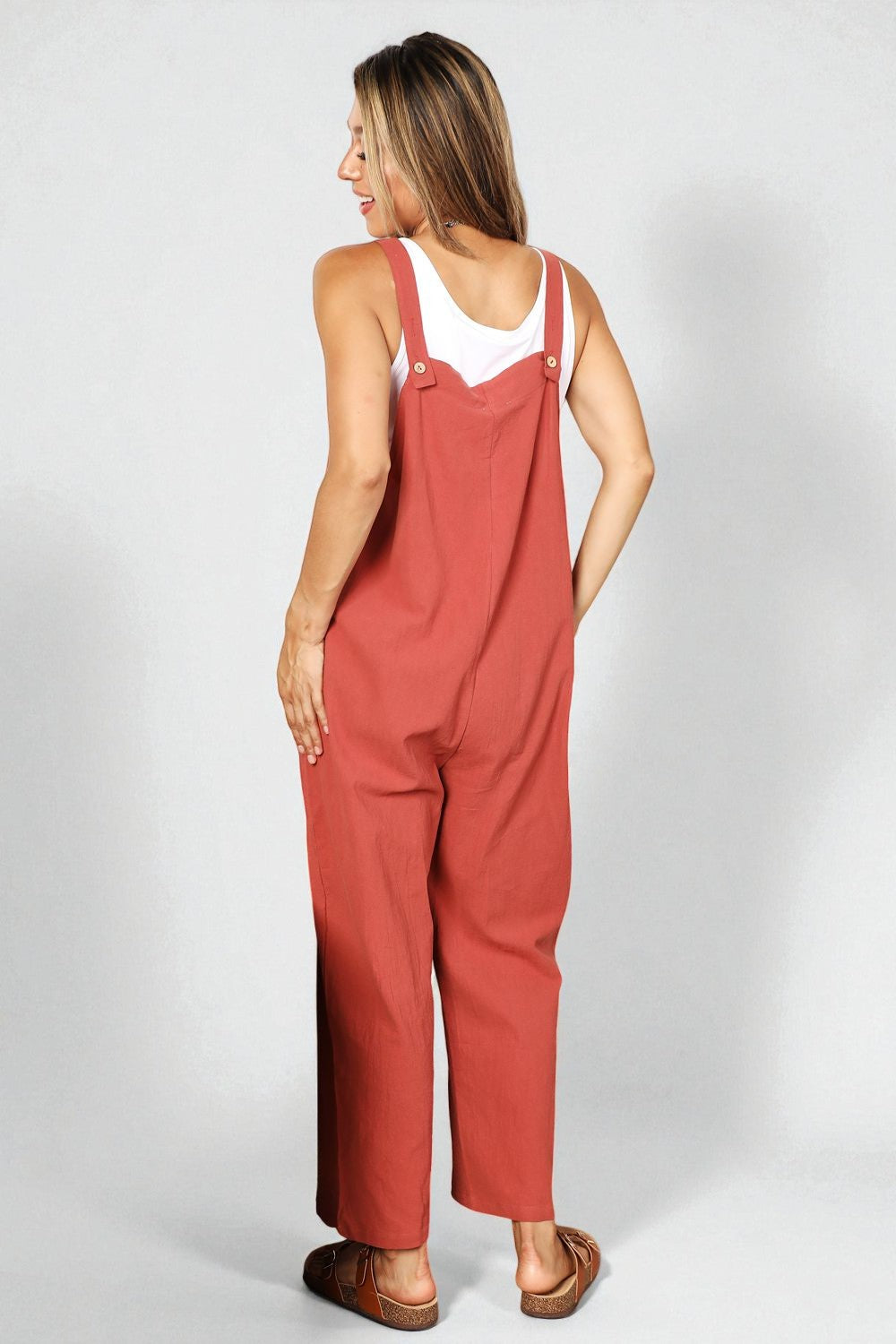 Woman wearing red overalls and a white tank top on a plain background