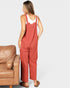 Woman wearing red overalls standing next to a brown leather chair on a plain background