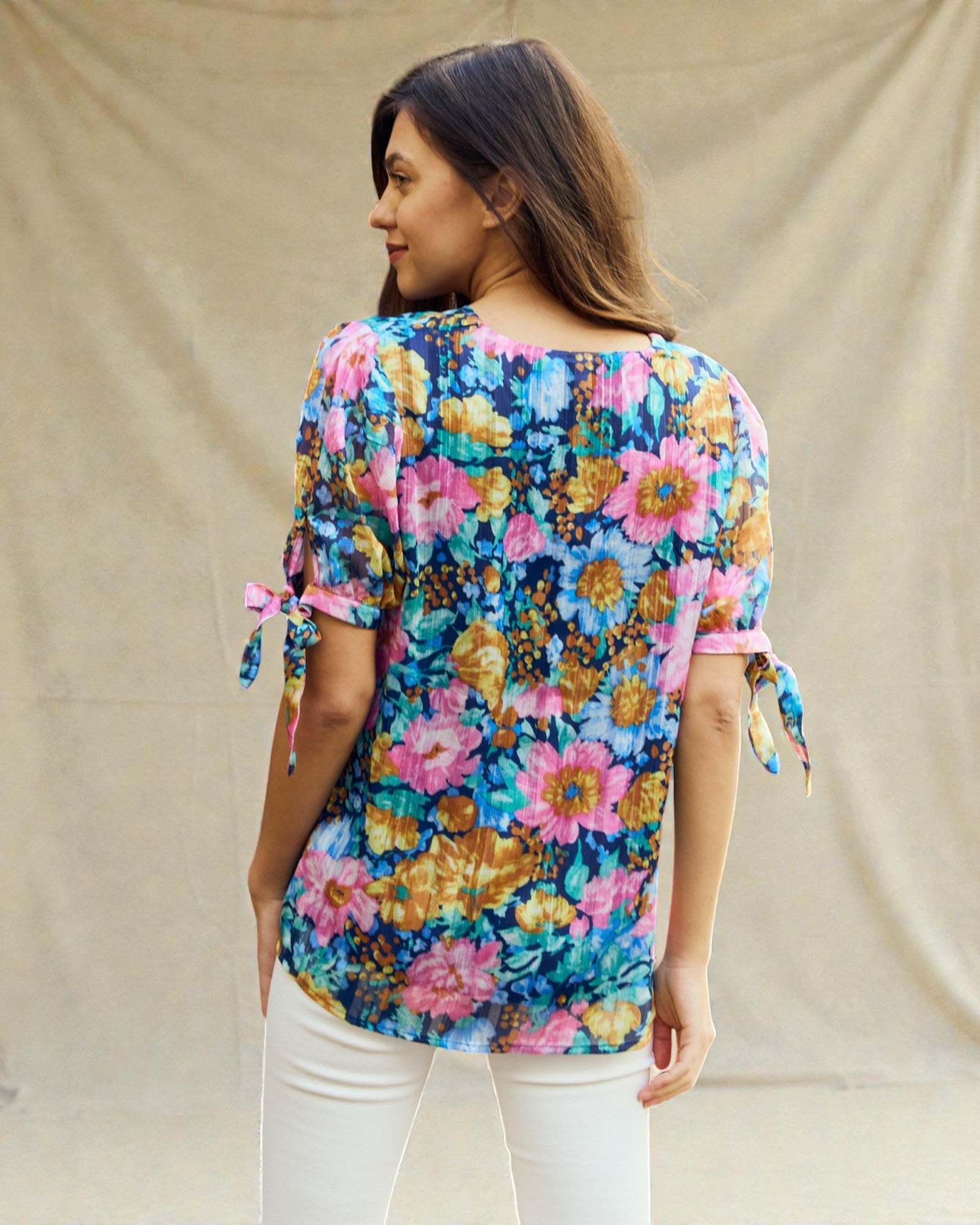 Woman wearing a colorful floral blouse with tied sleeves against a beige background