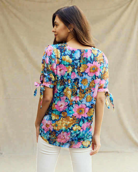 Woman wearing a colorful floral blouse with tied sleeves against a beige background