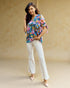 Woman wearing a colorful floral top and white pants against a beige background