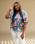 Woman wearing a colorful floral blouse and white pants against a beige background