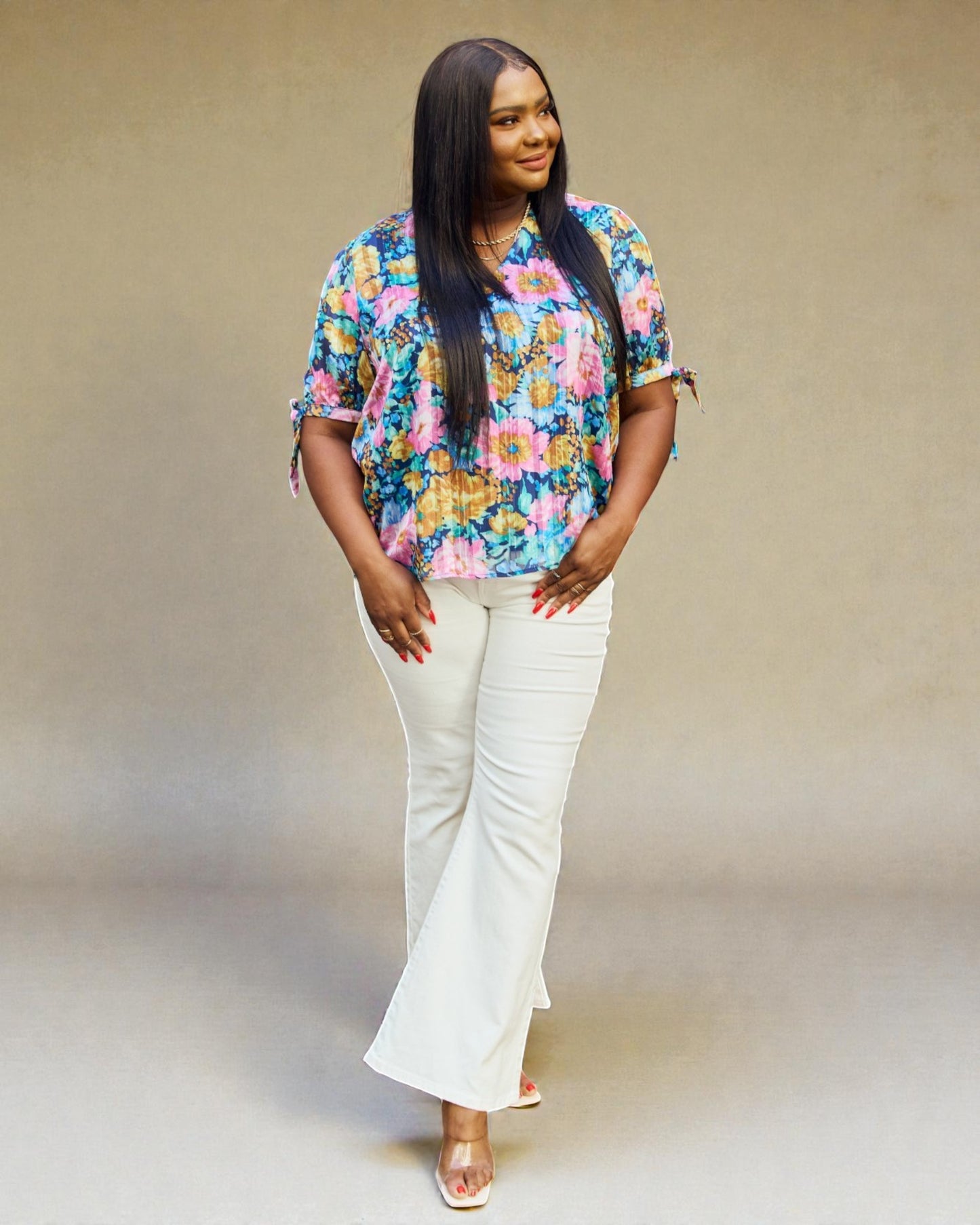 Woman wearing a colorful floral blouse and white pants against a plain background