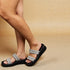 Black sandals with silver straps worn by a person on a beige background