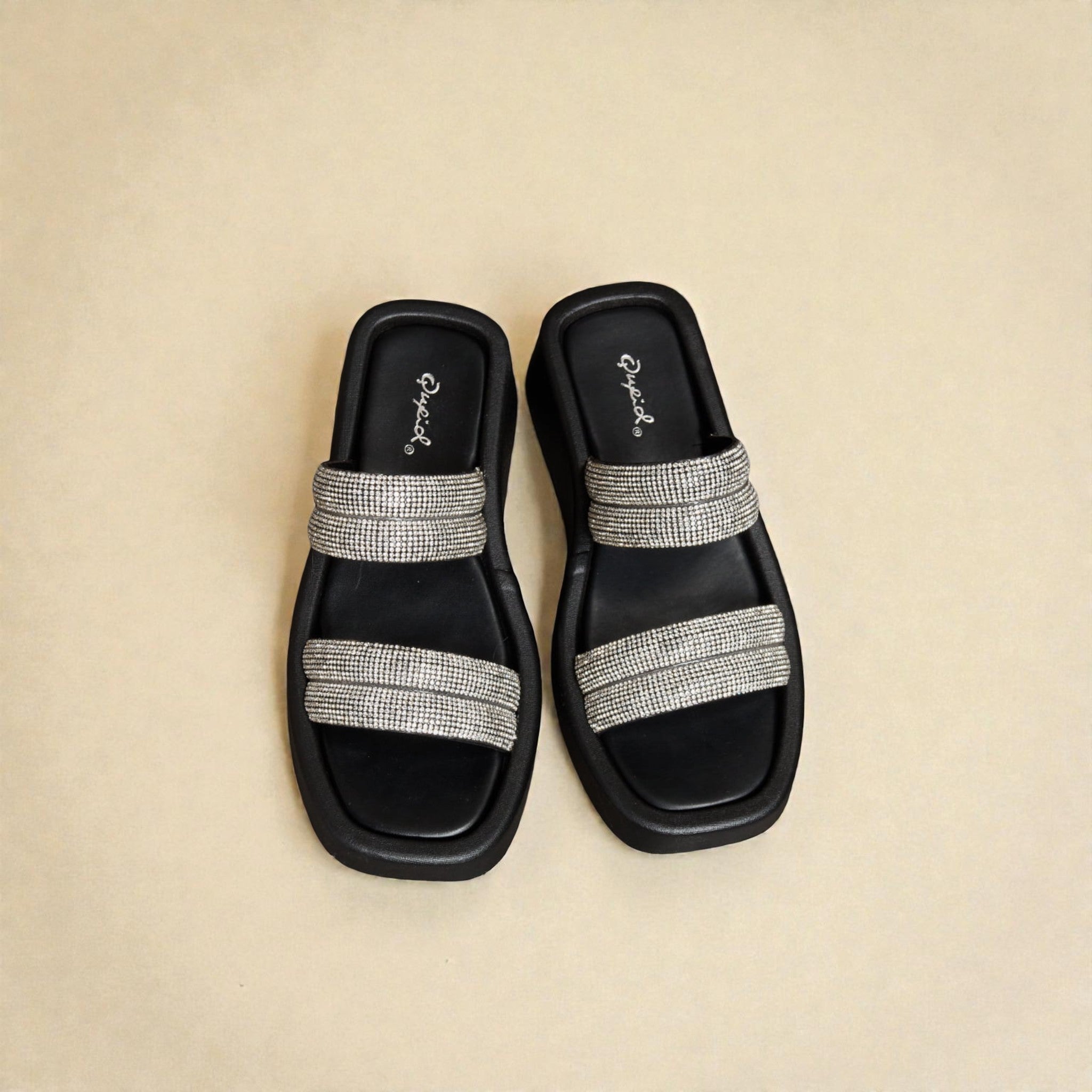 Black sandals with silver straps on a beige background