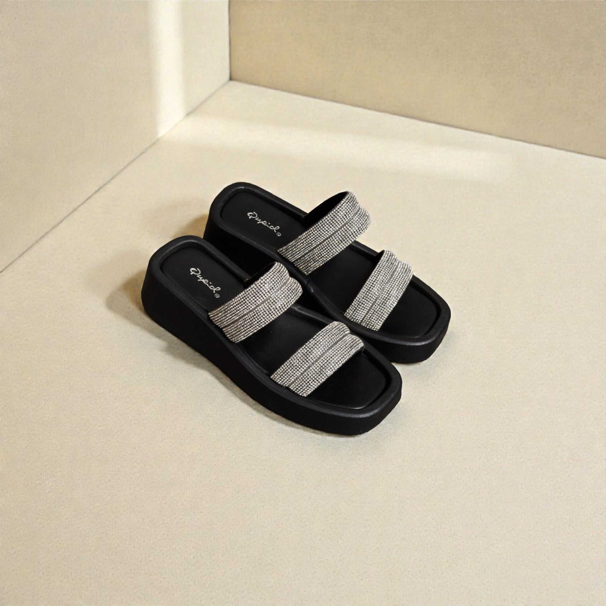 Black slides with silver straps on a beige surface