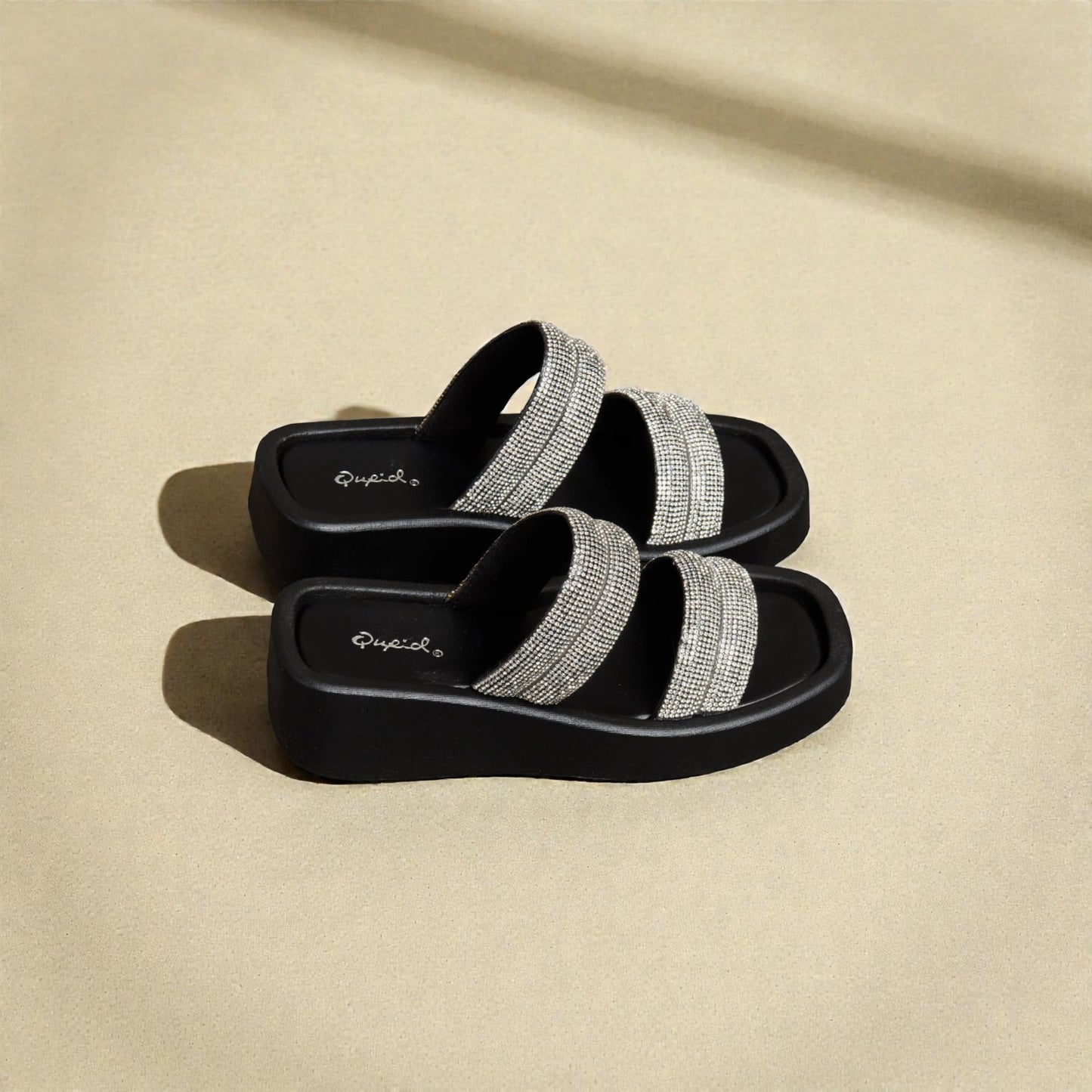 Black sandals with silver straps on a beige background