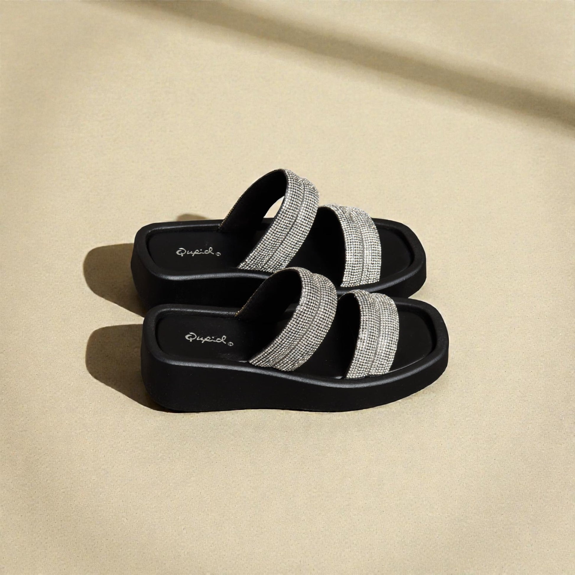 Black sandals with silver straps on a beige background
