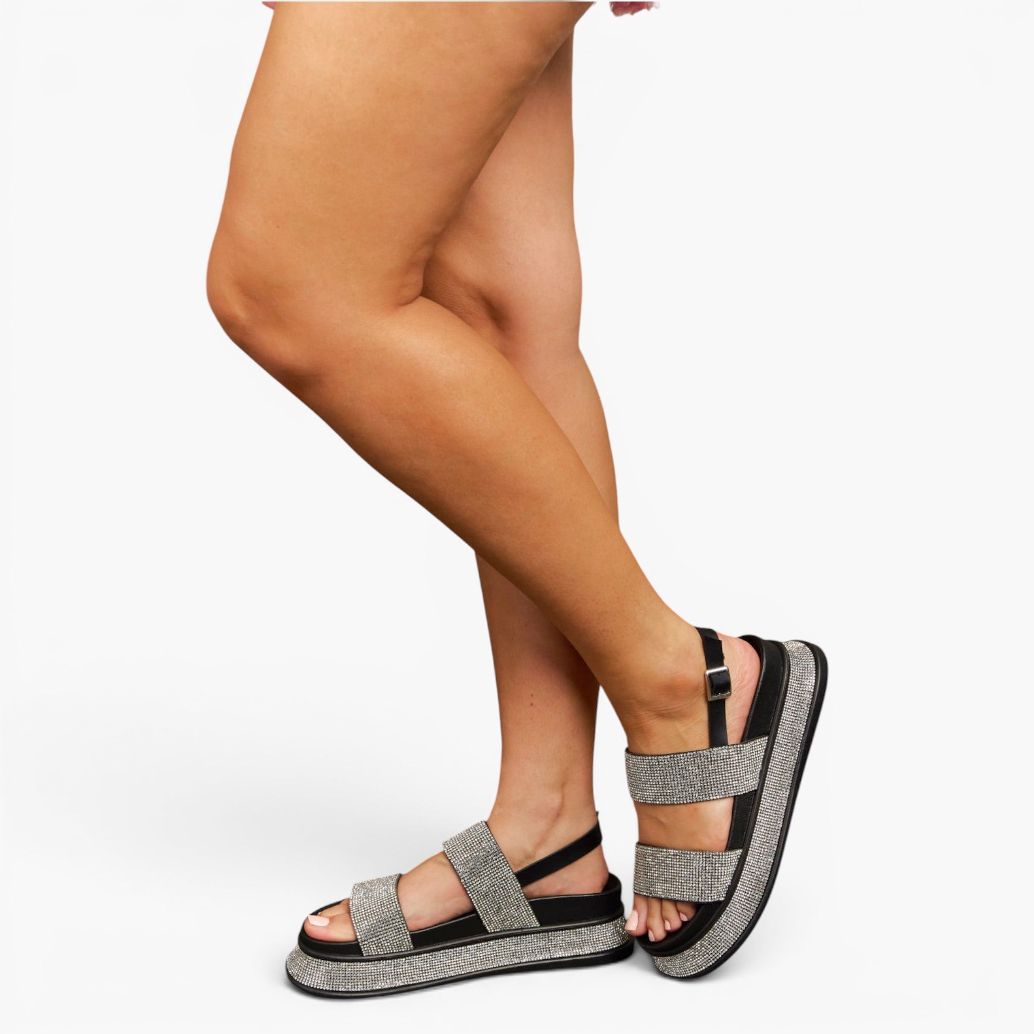 A person wearing open-toe platform sandals with wide gray glittery straps and black ankle straps, shown against a plain light gray studio background.