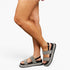 A person wearing open-toe platform sandals with wide gray glittery straps and black ankle straps, shown against a plain light gray studio background.