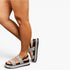 A person wearing glittery silver platform sandals with black straps and buckles, shown against a plain light gray studio background.