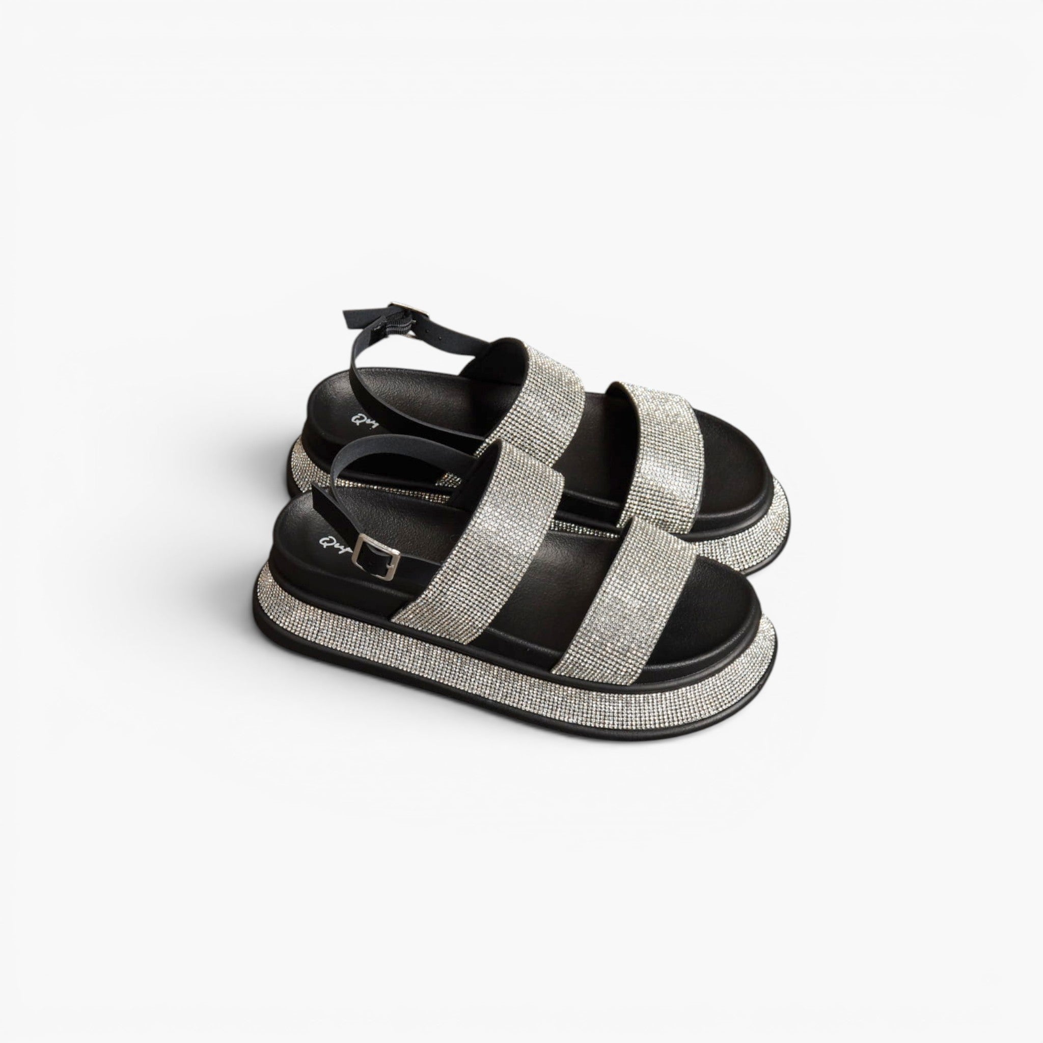 A pair of platform sandals with wide, sparkling silver glitter straps and black soles, displayed on a clean white background.