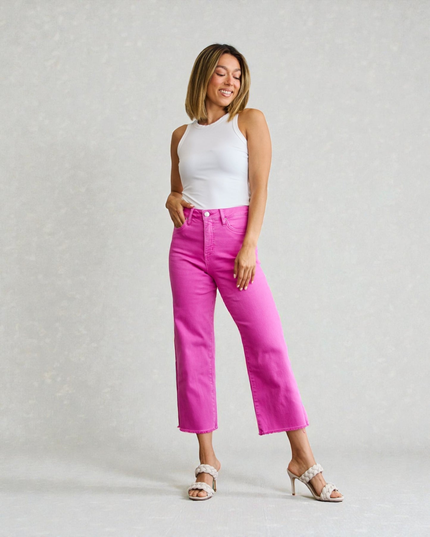 Woman wearing a white sleeveless top and bright pink pants on a light gray background