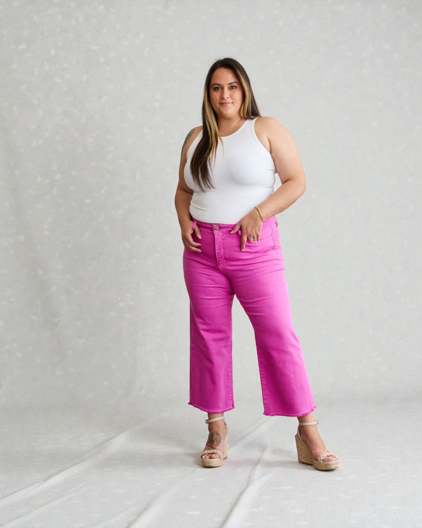 Woman wearing a white tank top and pink pants on a plain background
