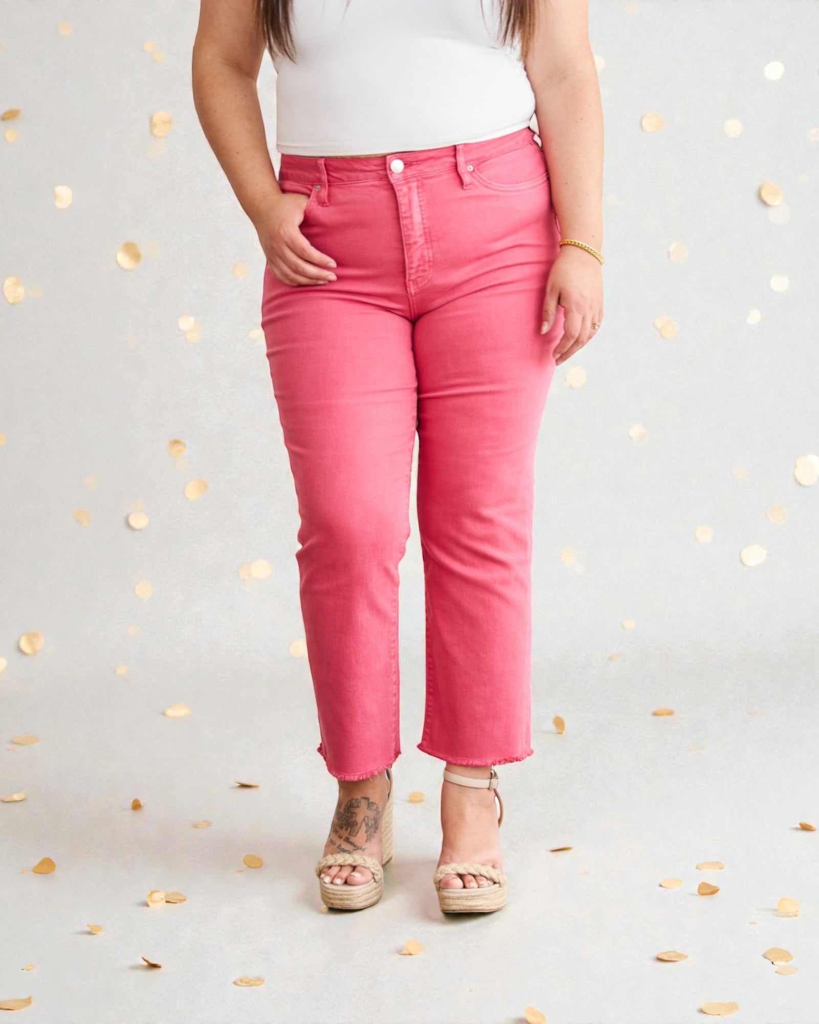 Person wearing bright pink jeans on a light gray background with gold leaf decorations