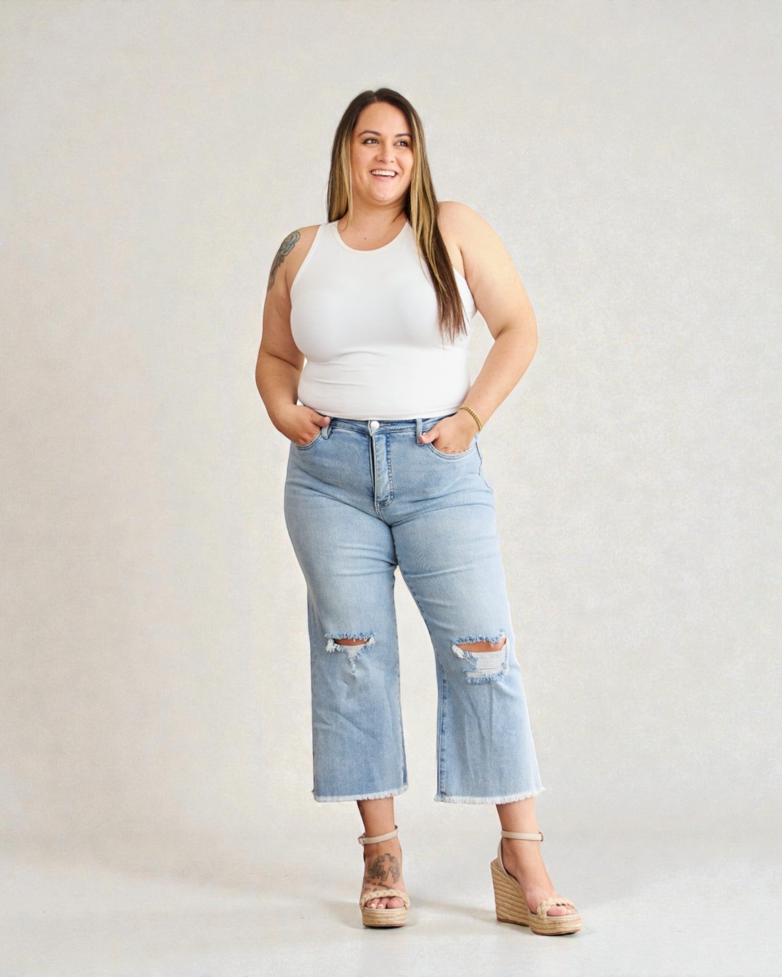 Woman wearing a white tank top and light blue jeans with a gray background
