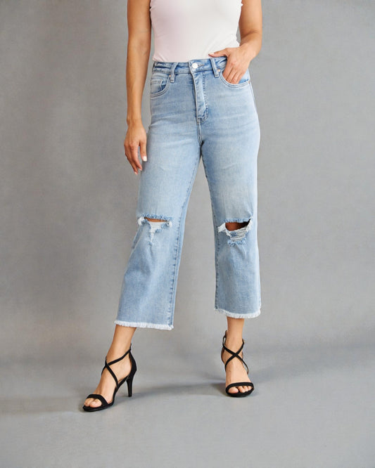 Person wearing light blue ripped jeans on a gray background