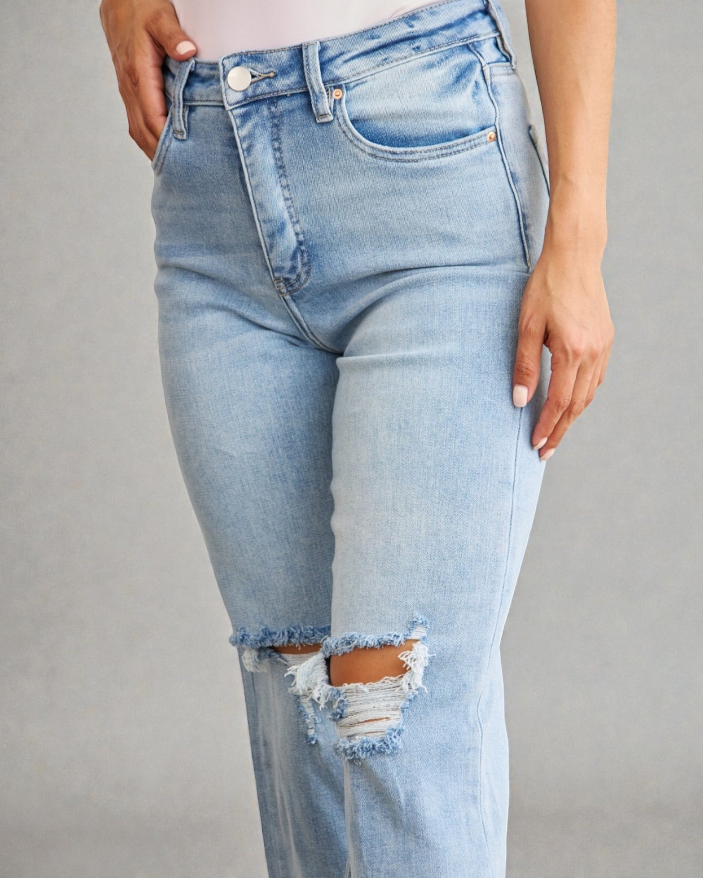 Light blue jeans with a distressed knee on a gray background