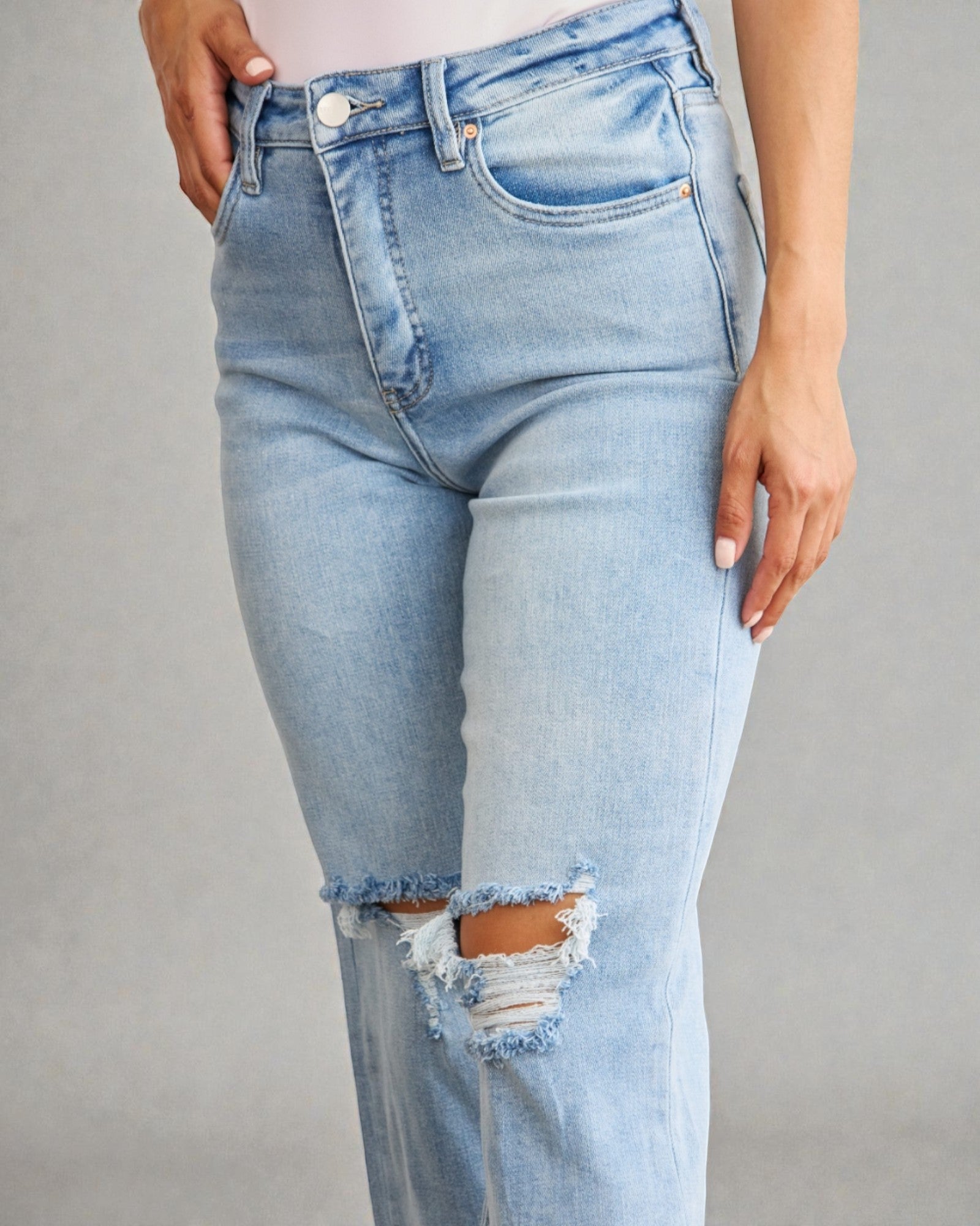 Light blue jeans with a distressed knee on a gray background