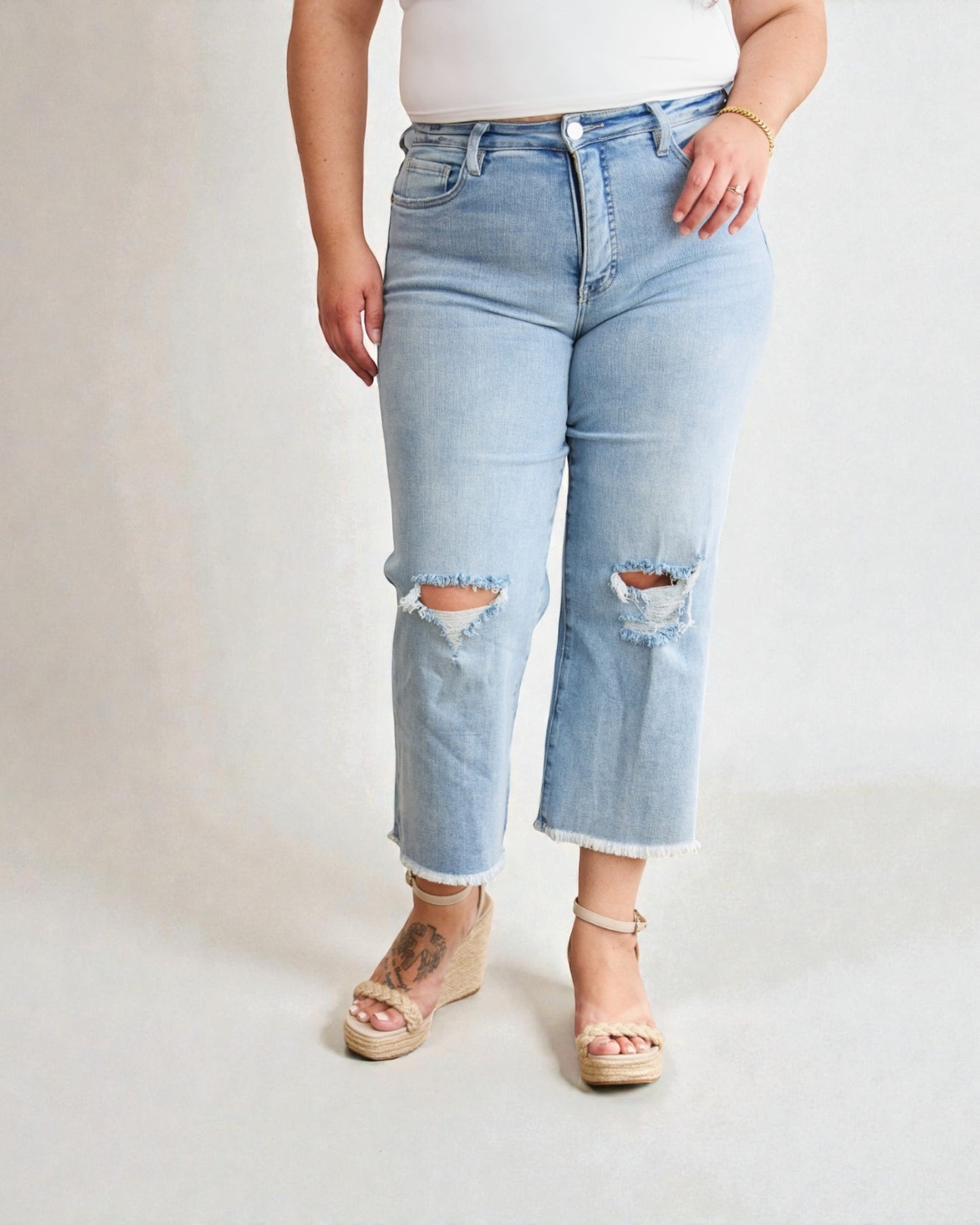 Person wearing light blue ripped jeans on a plain background