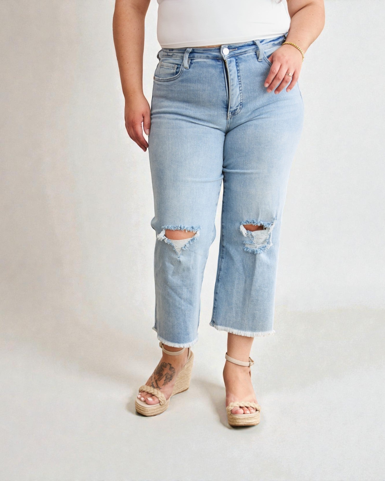 Person wearing light blue ripped jeans on a plain background