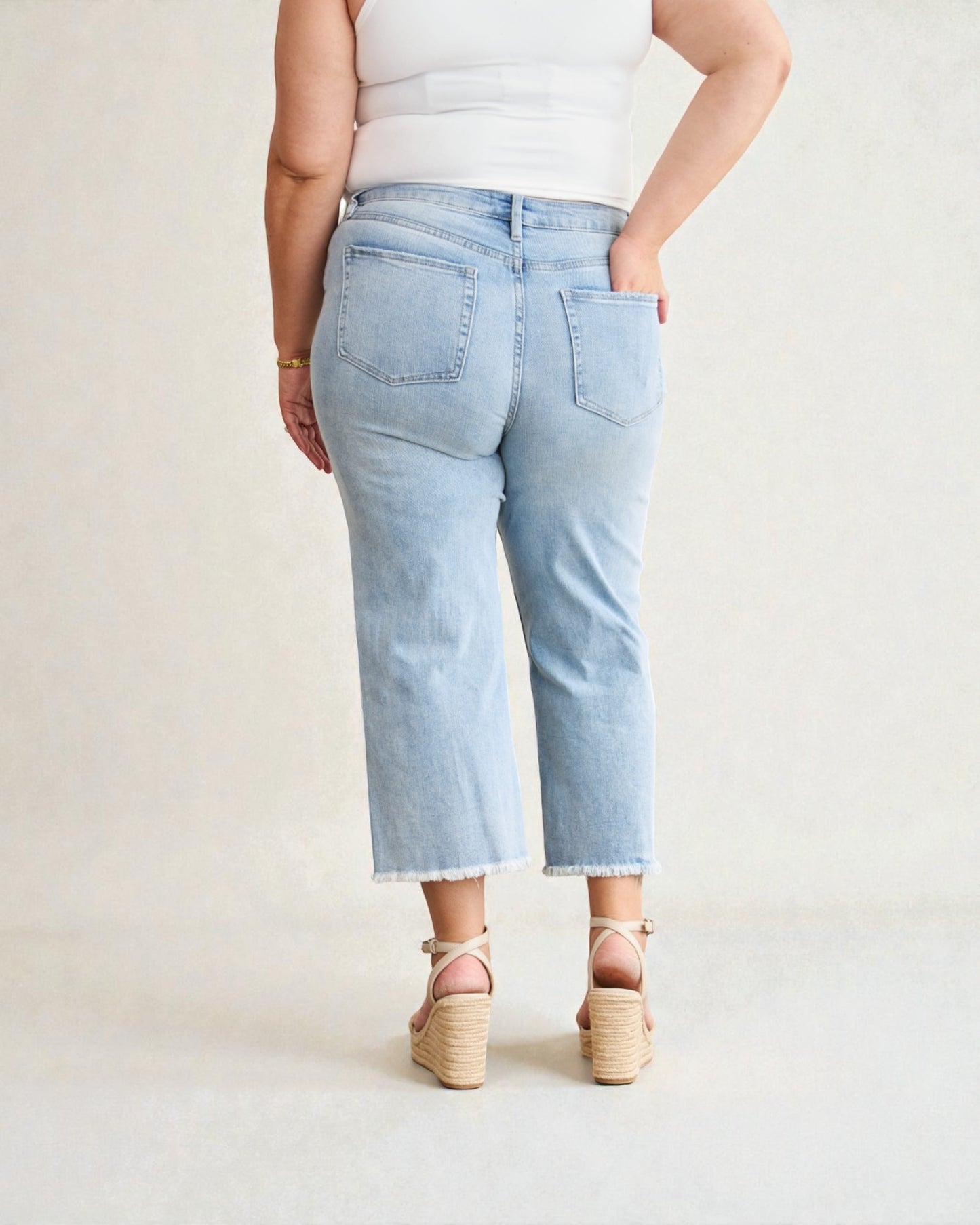 Person wearing light blue jeans and a white top on a plain background