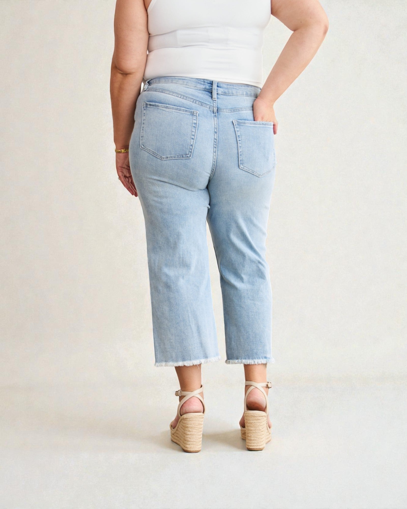 Person wearing light blue jeans and a white top on a plain background