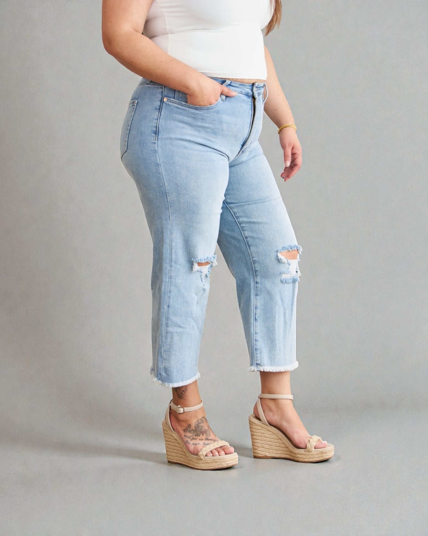Person wearing light blue distressed jeans and beige sandals on a gray background