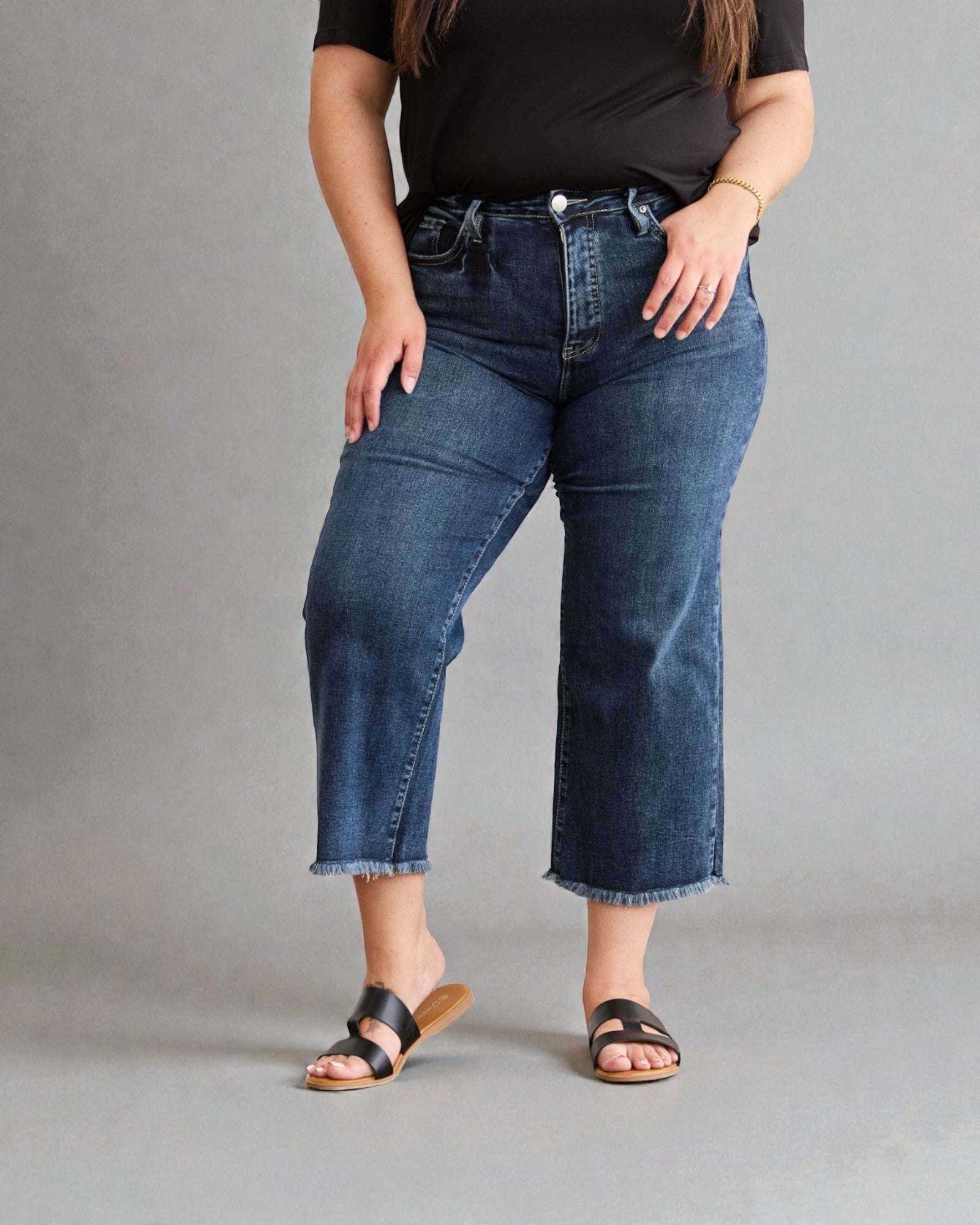 Person wearing blue jeans and a black top on a gray background