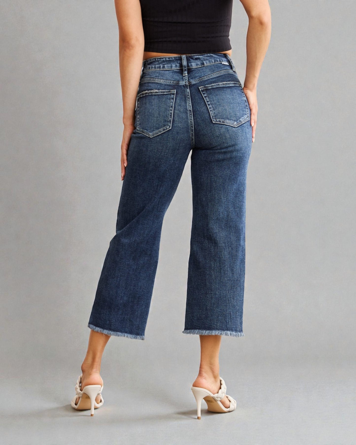 Person wearing blue jeans and a black top on a gray background