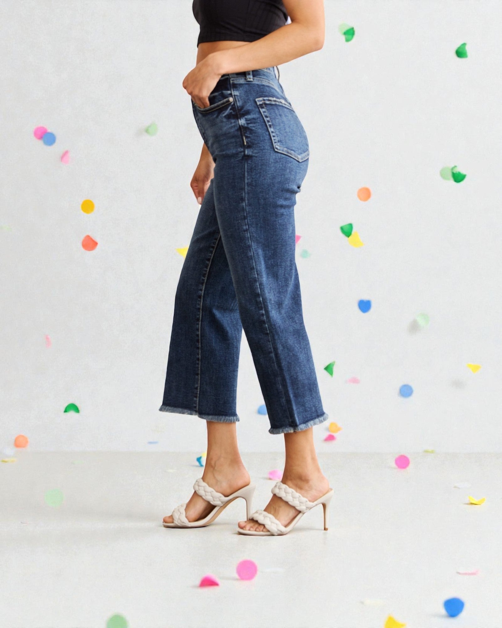 Person wearing blue jeans with a light gray background and colorful confetti