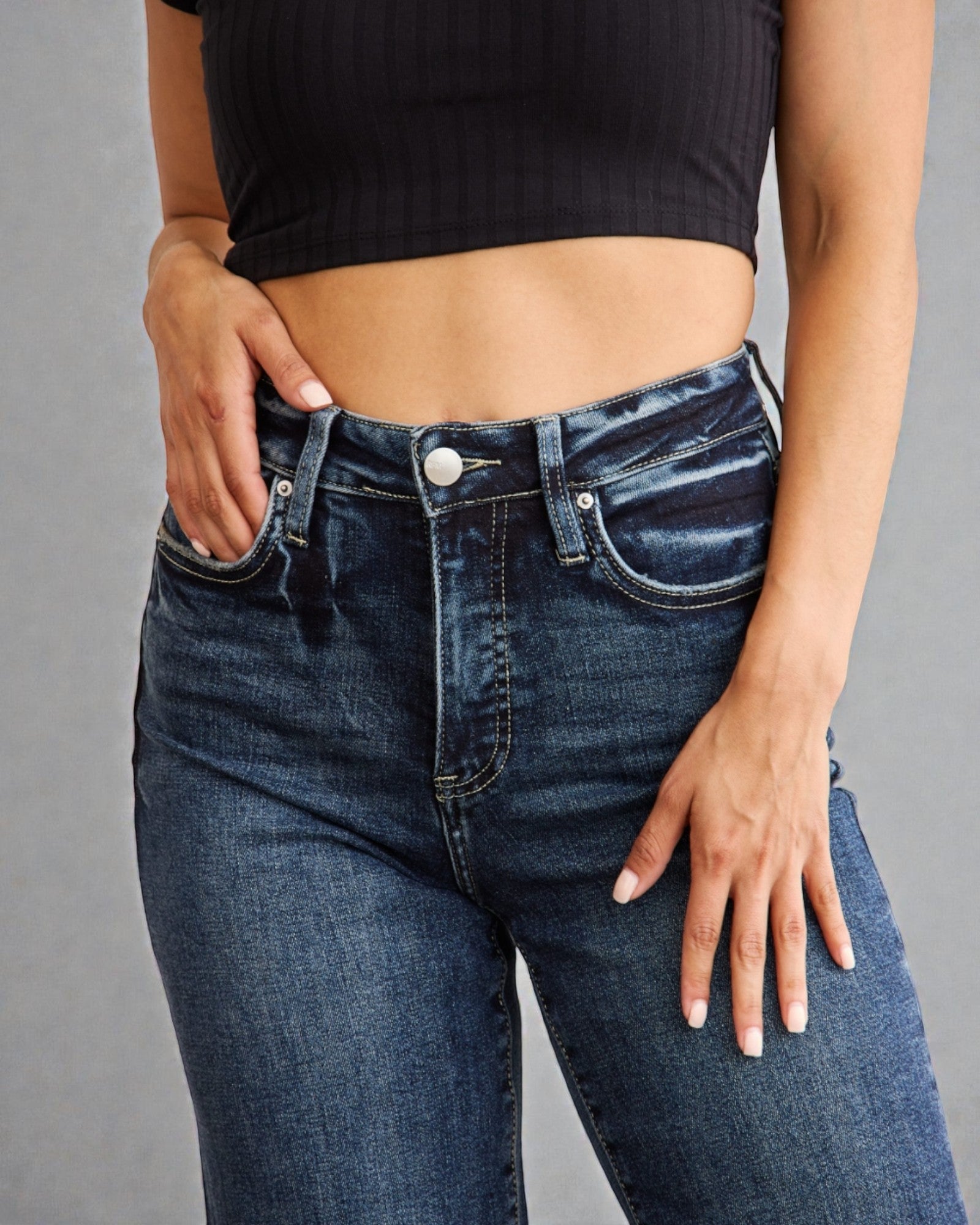 Person wearing blue jeans and a black crop top on a gray background