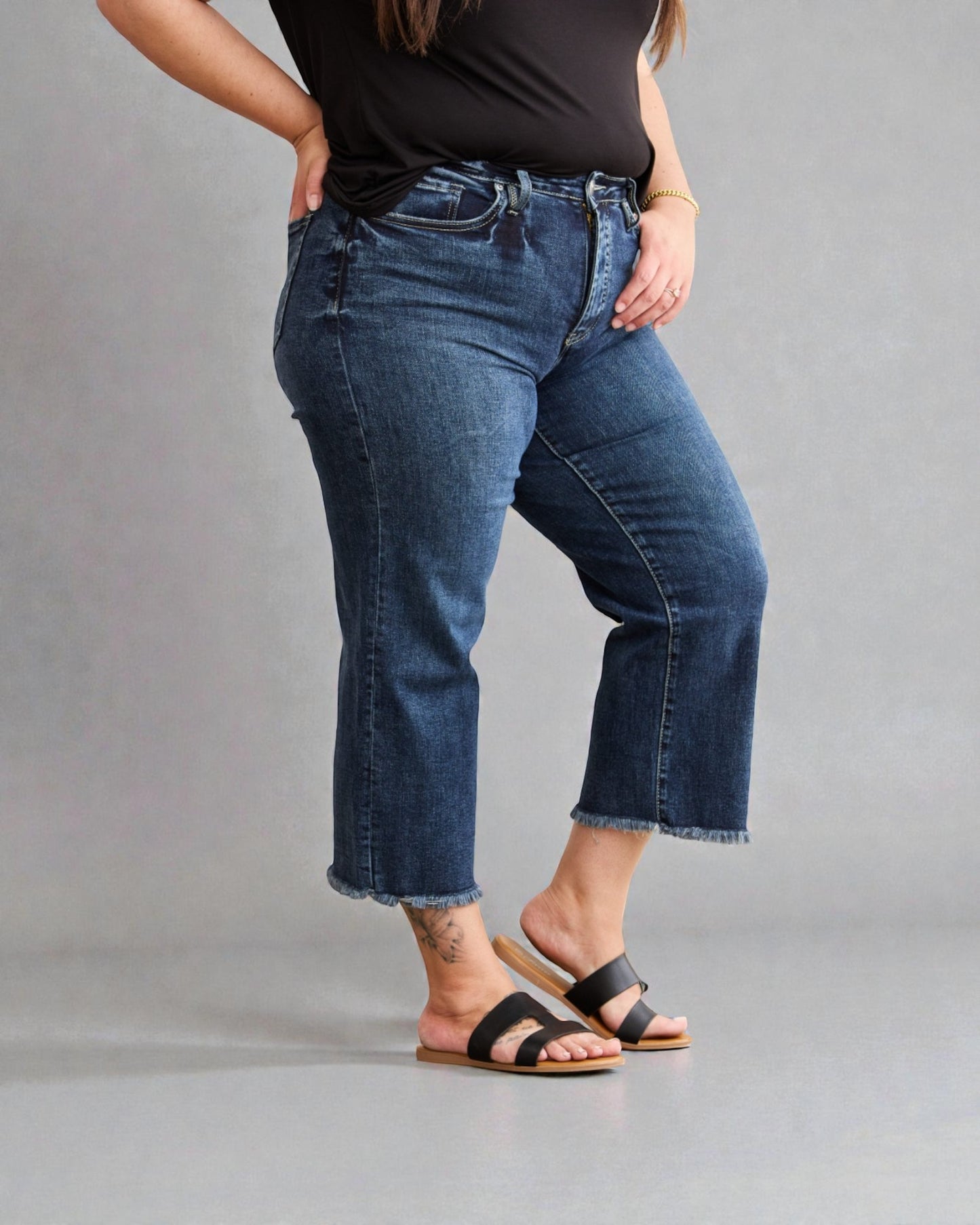 Person wearing blue jeans and black sandals on a gray background