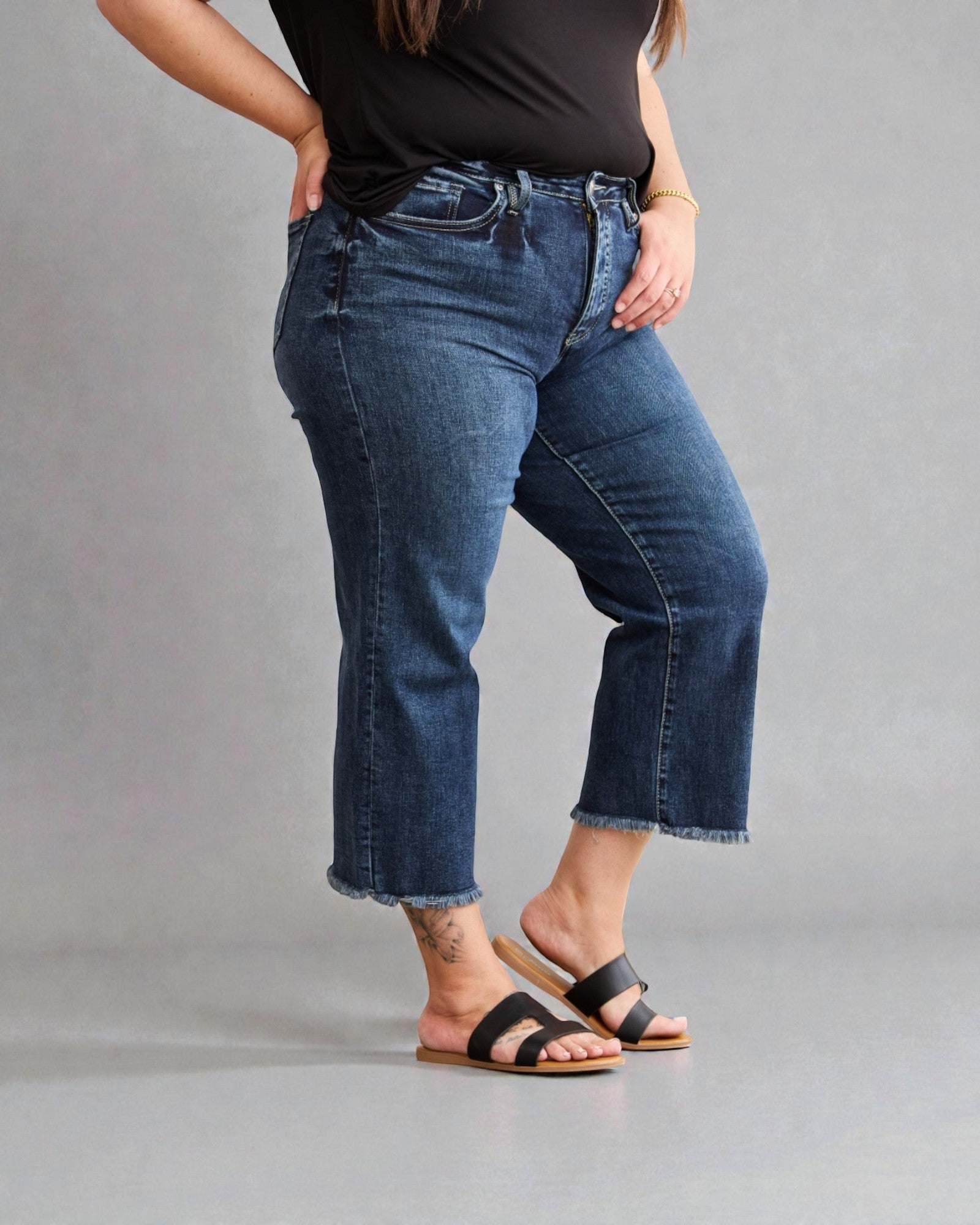 Person wearing blue jeans and black sandals on a gray background