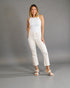 Woman wearing a white sleeveless top and white pants against a gray background