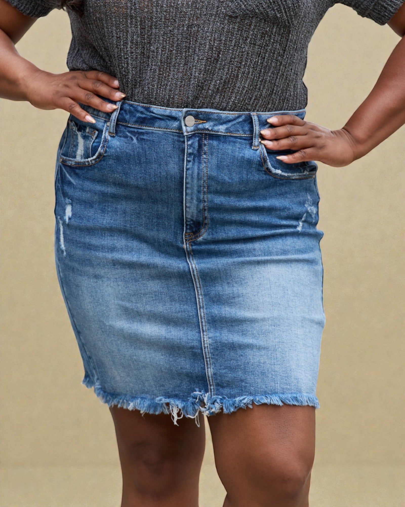Person wearing a blue denim skirt and dark gray top against a beige background