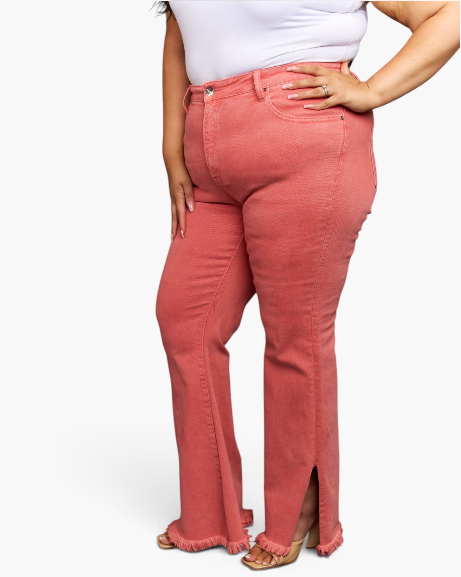 A model wearing a pair of dusty rose flare jeans with side slits and frayed hems, paired with a white top and tan heeled sandals, shown from the waist down against a plain white background.