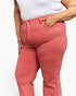 A close-up of a person wearing coral pink denim jeans with a white top, showing the side and back pocket details against a plain white background.
