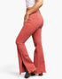 A model wearing a pair of high-waisted, flared denim jeans in a faded coral pink color, shown from a side-back angle against a clean white background.