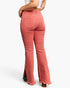 Rear view of a model wearing high-waisted, flared jeans in a dusty coral pink color, paired with a white crop top and brown heels, against a plain white studio background.