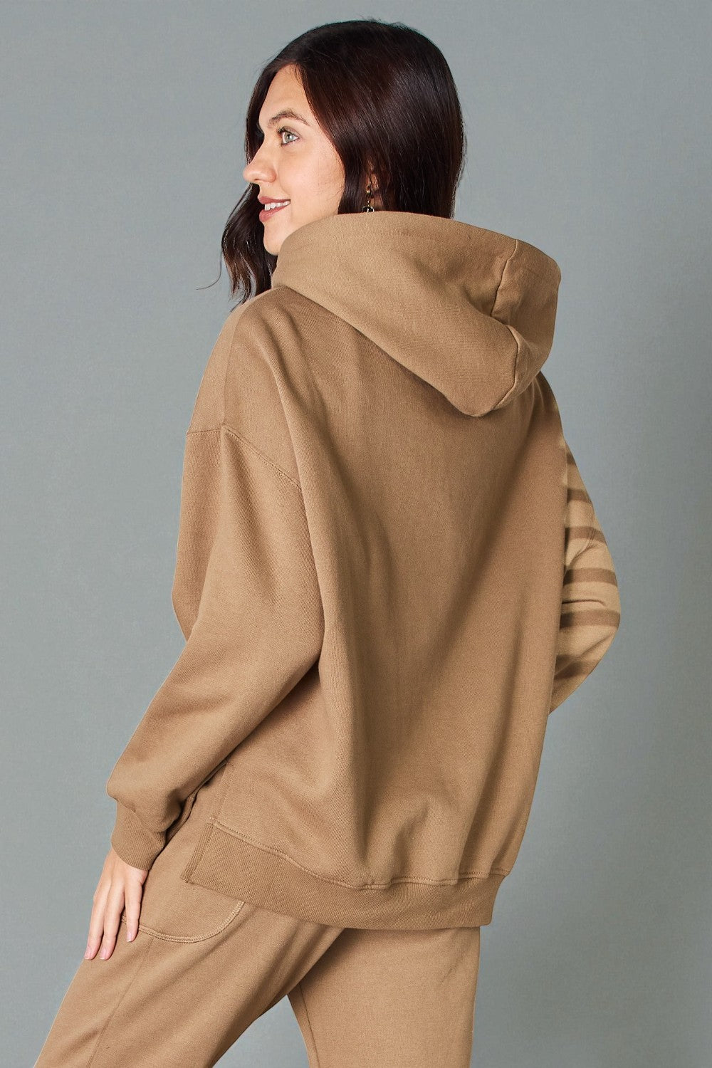 Woman wearing a brown hoodie and pants against a gray background