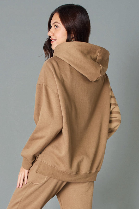 Woman wearing a brown hoodie and pants against a gray background