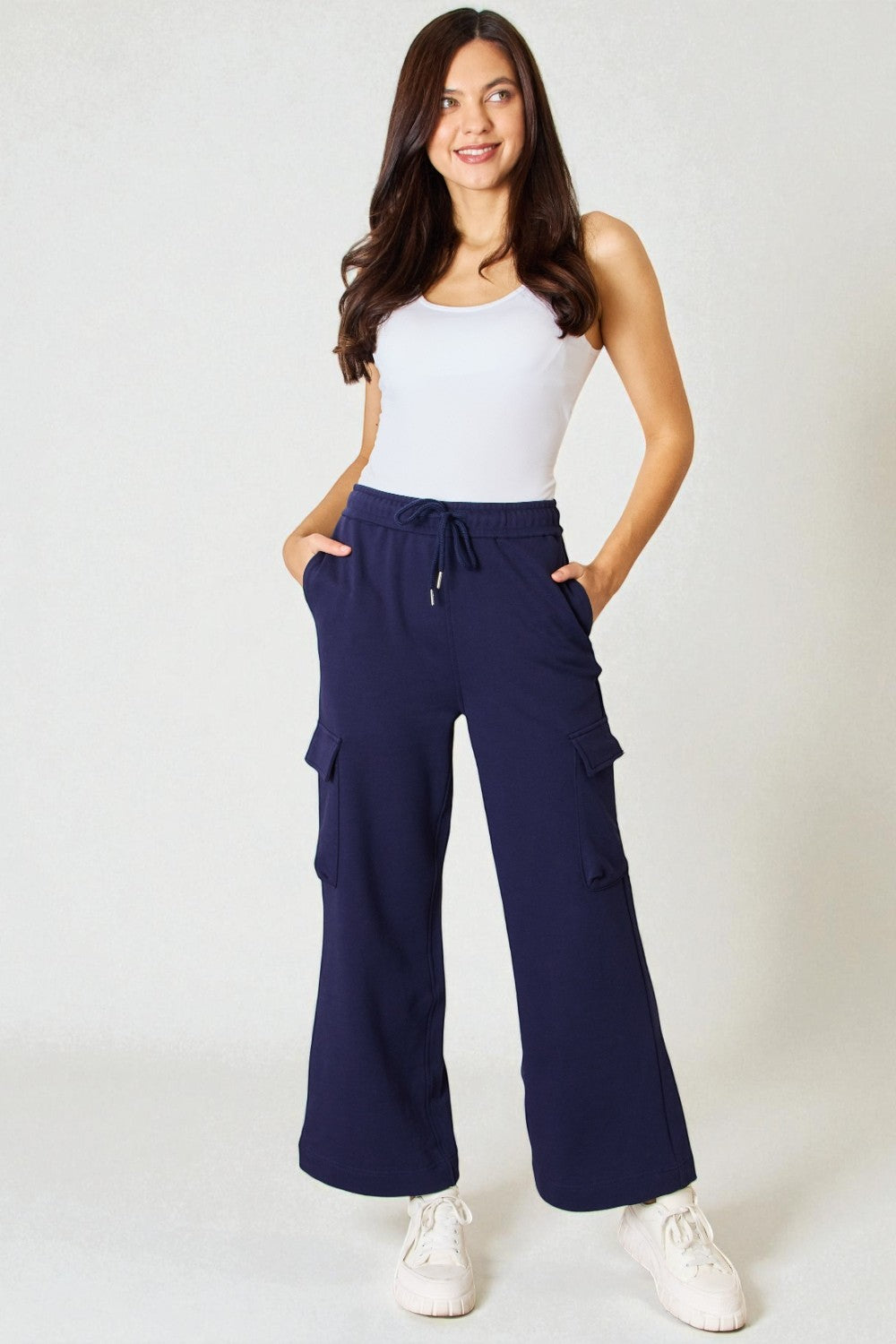 Woman wearing navy cargo pants and a white top on a plain background