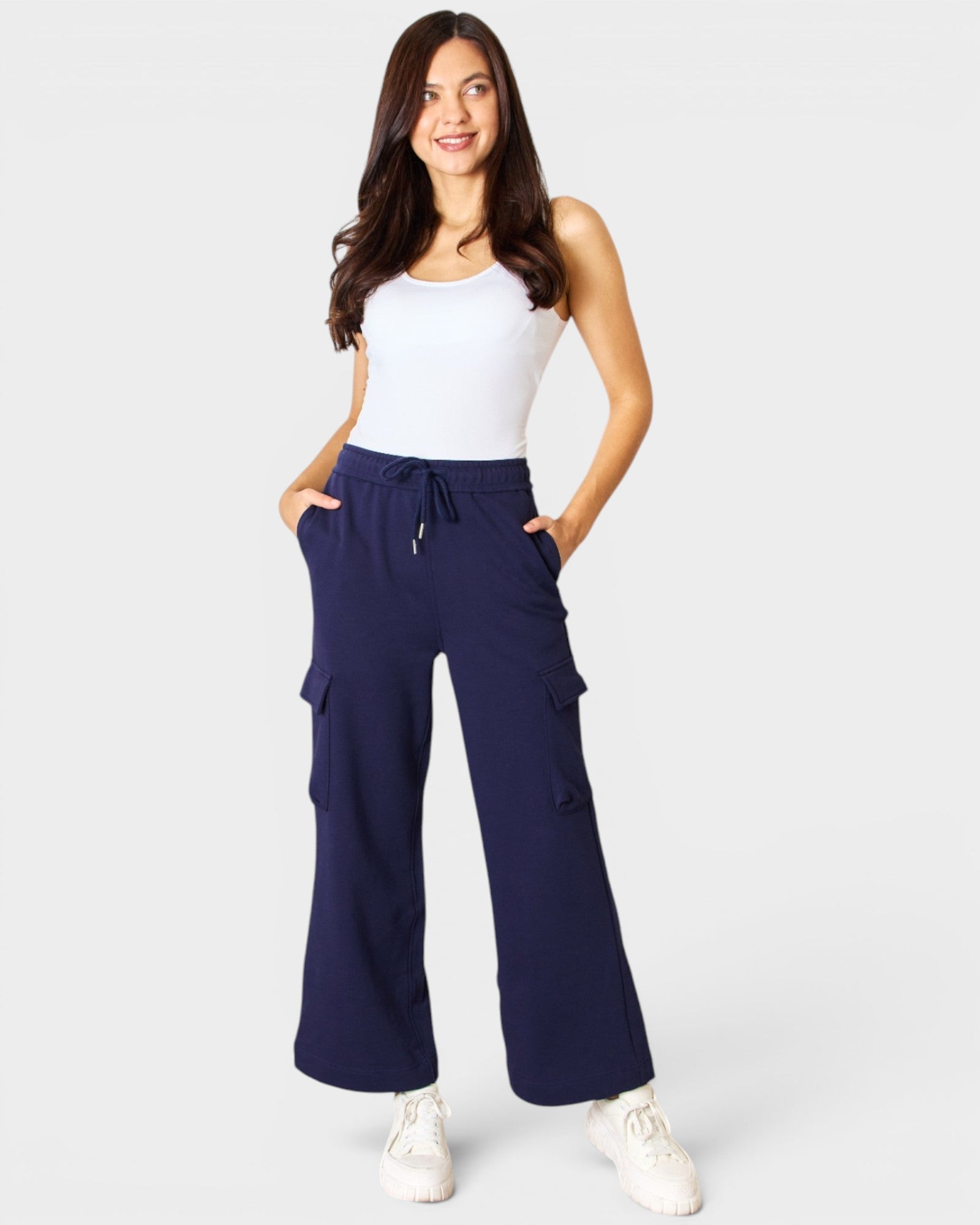 Woman wearing navy cargo pants and a white top on a light gray background