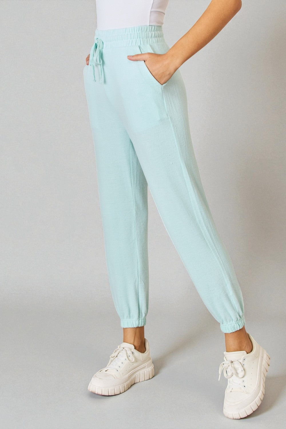 Person wearing light blue jogger pants and white sneakers on a plain background